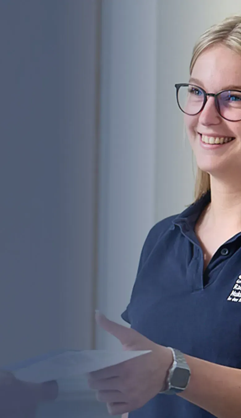 Mitarbeiterin der Praxis für Radiologie und Nuklearmedizin in der Kaiser-Passage übergibt einem Patienten freundlich Unterlagen am Empfang.