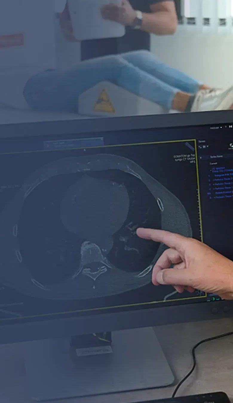 Radiologe der Praxis für Radiologie und Nuklearmedizin in der Kaiser-Passage bespricht eine CT-Aufnahme mit einer Kollegin, im Hintergrund liegt eine Patientin im Untersuchungsraum.